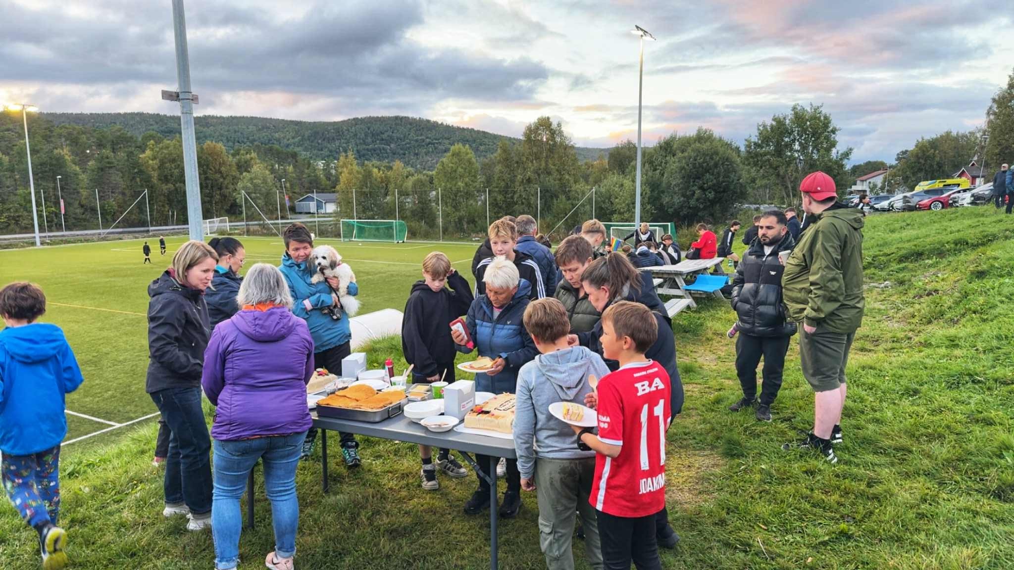 Barn og voksne samlet rundt matbordet ved fotballbanen